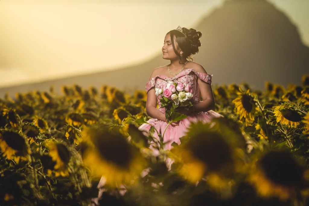 Woman in a pink ballgown and tiara holding a bouquet of flowers in a sunflower field